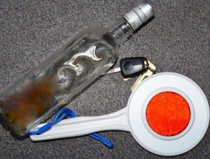 Zdjęcie przedstawia butelkę z alkoholem, kluczyki do samochodu oraz tak zwany lizak policyjny.