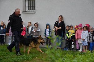 Zdjęcie przedstawia przedszkolaków oraz policjanta z psem policyjnym.