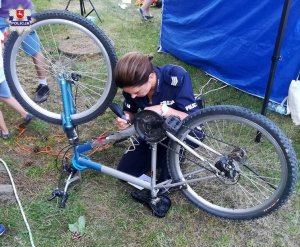 Zdjęcie przedstawia policjantkę naprawiającą rower.