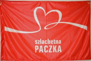 Zdjęcie przedstawia flagę z napisem &quot;Szlachetna Paczka&quot;.