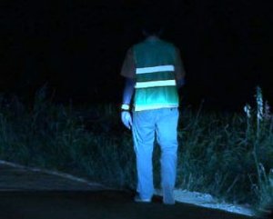 Zdjęcie przedstawia mężczyznę idącego nocą w kamizelce odblaskowej.