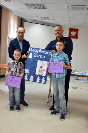 Zdjęcie przedstawia dwójkę chłopców z dyplomami, Komendanta wraz z przedstawicielem starosty, którzy trzymają plakat &quot;Bezpieczna Zima&quot;.