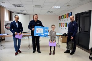 Zdjęcie przedstawia dziewczynkę z dyplomem oraz Komendanta wraz z przedstawicielem starosty oraz funkcjonariuszem Policji.